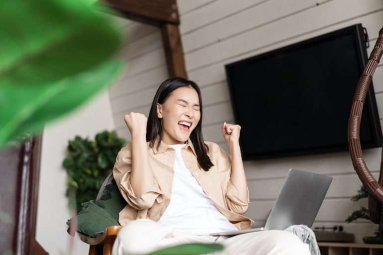 Joyful asian woman winning online on laptop, celebrating victory, shouting and rejoicing, triumphing
